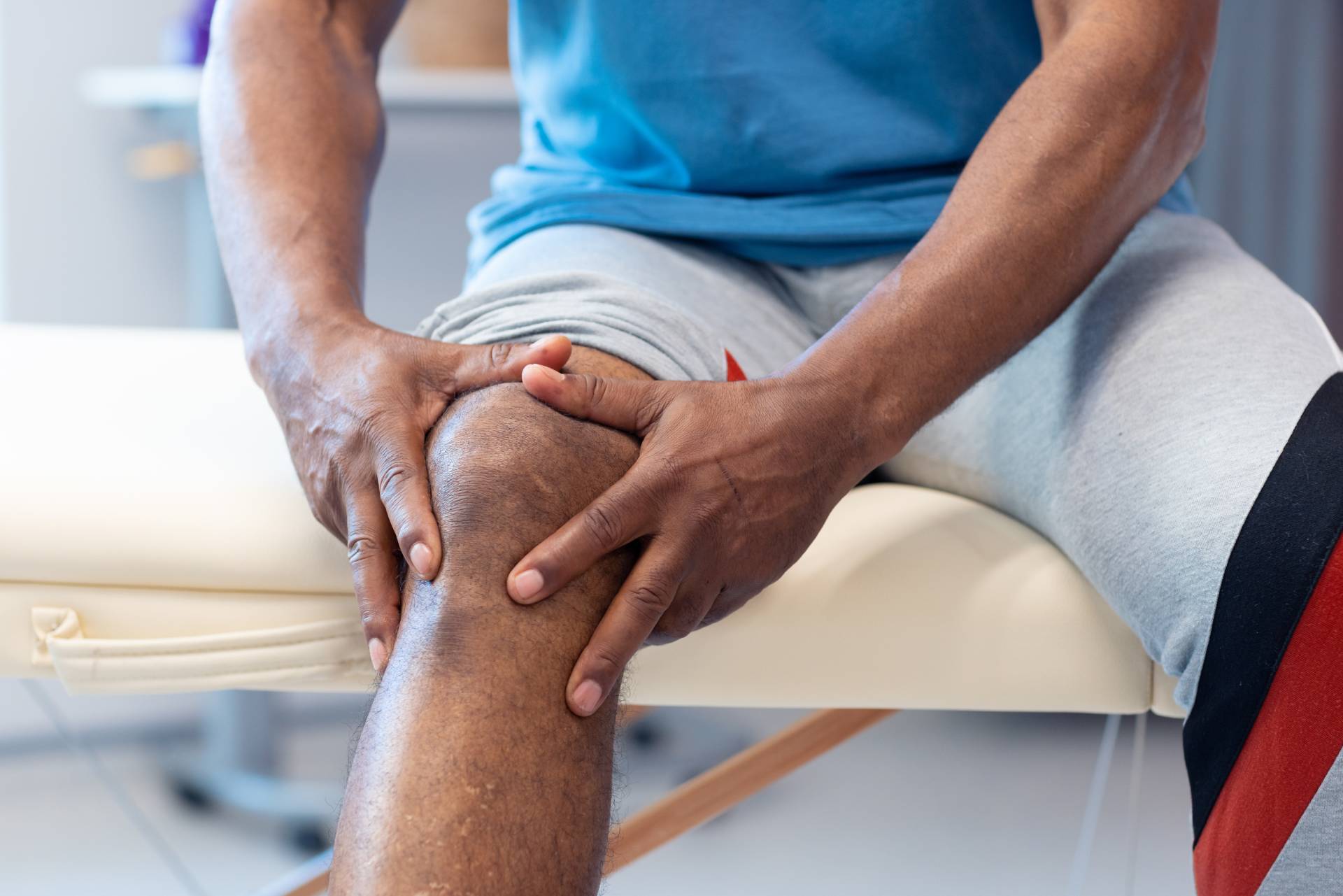 Midsection of senior african american male patient holding knee in physiotherapy session, copy space. Hospital, medical and healthcare services.
