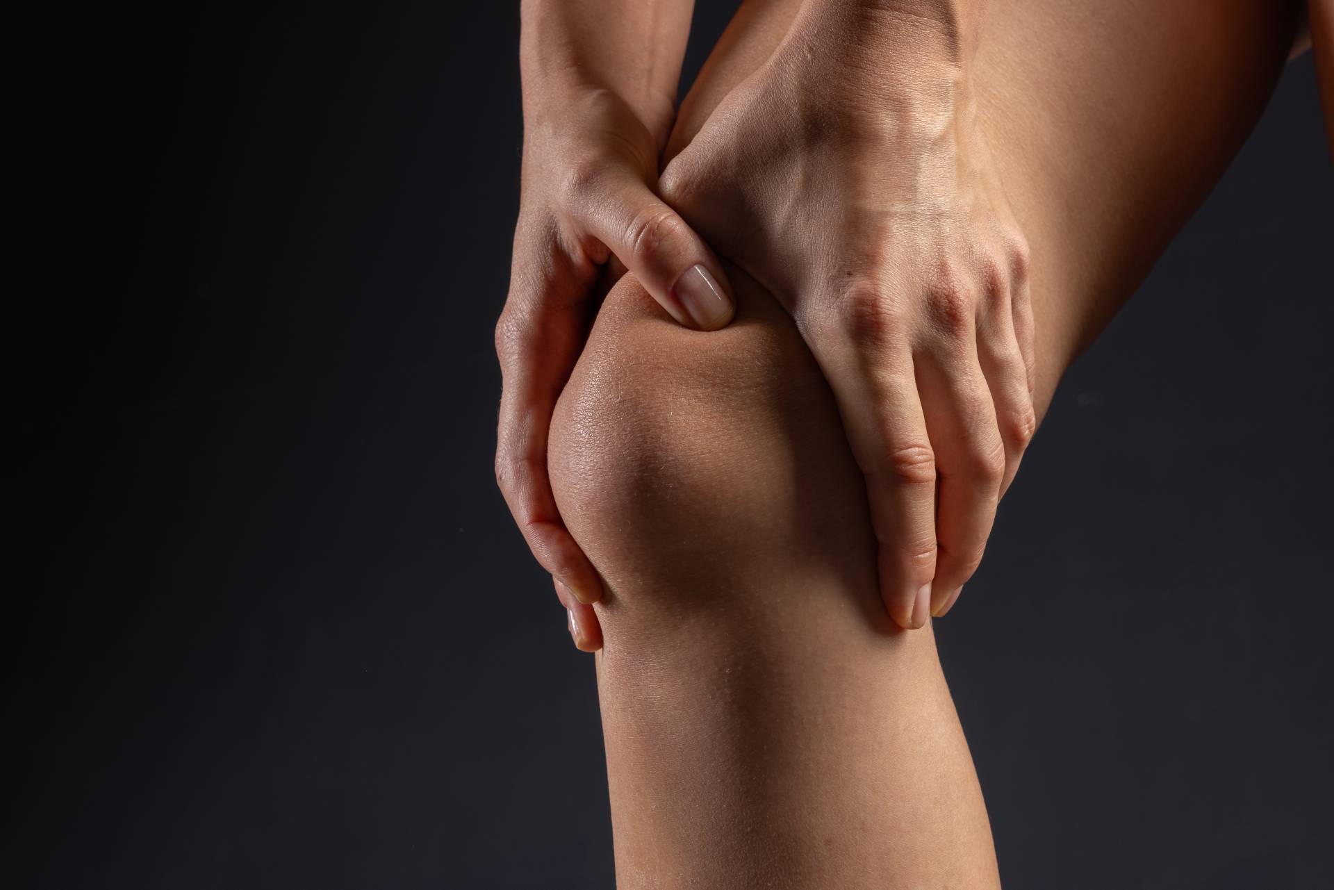 woman hands close up pressing on knee joint on dark background, knee pain concept