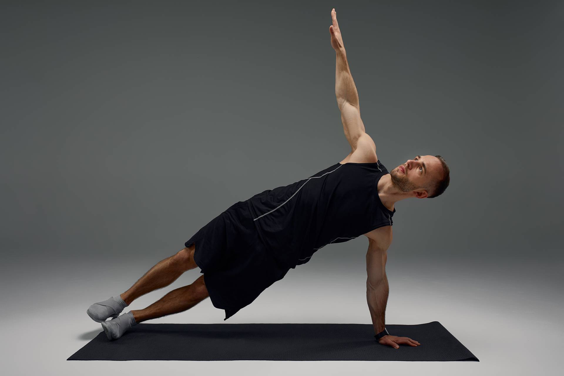 Attractive healthy young sports man stretching on fitness mat indoors, over gray wall background
